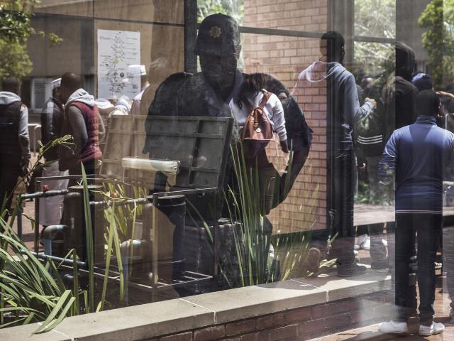 A police officer checking his phone is reflected in a window as students from the University of Witwatersrand's medical school gather after clashes during a protest for free high education in October 2016 in Johannesburg, South Africa. Photo: AFP/GIA