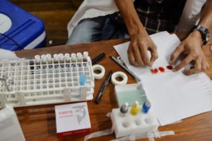 An Indian blood bank official tests a slide covered with a blood sample as he checks a donor's blood group in Salugara Monestry on the outskirts of Siliguri on May 10, 2019. - Some 50 donors as well as monks donated blood due to a shortage on the blood banks. (Photo by DIPTENDU DUTTA / AFP)