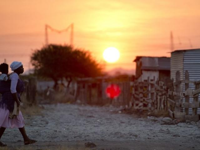 A woman carries her child as the sun sets in the informal settlement of Nkaneng next to Lonmin's platinum smelter in Marikana in July 2013. Photo: AFP/Odd Andersen