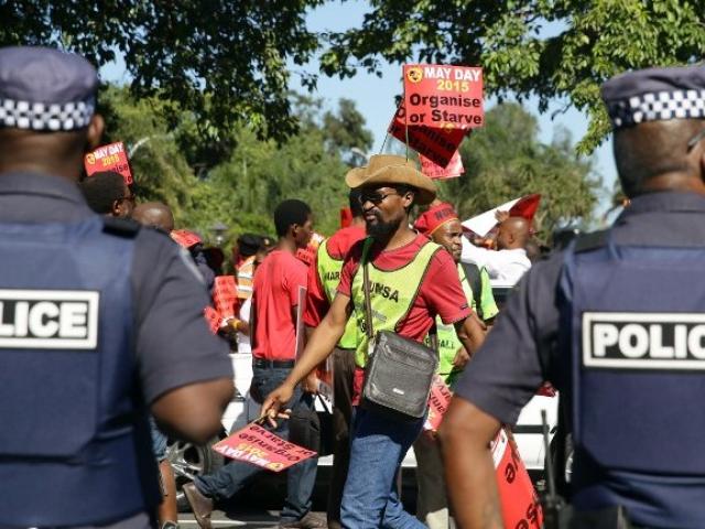 South African policemen stand guard as thousands of workers from several unions, under the leadership of the National Union of Mineworkers of South Africa (NUMSA) and the United Front, take part in a march to celebrate Labour Day in central Durban on