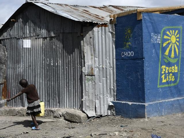 Une jeune fille portant un jerrican d'eau passe devant des toilettes installées dans le bidonville de Mukuru à Nairobi, le 8 août 2019. SIMON MAINA/AFP